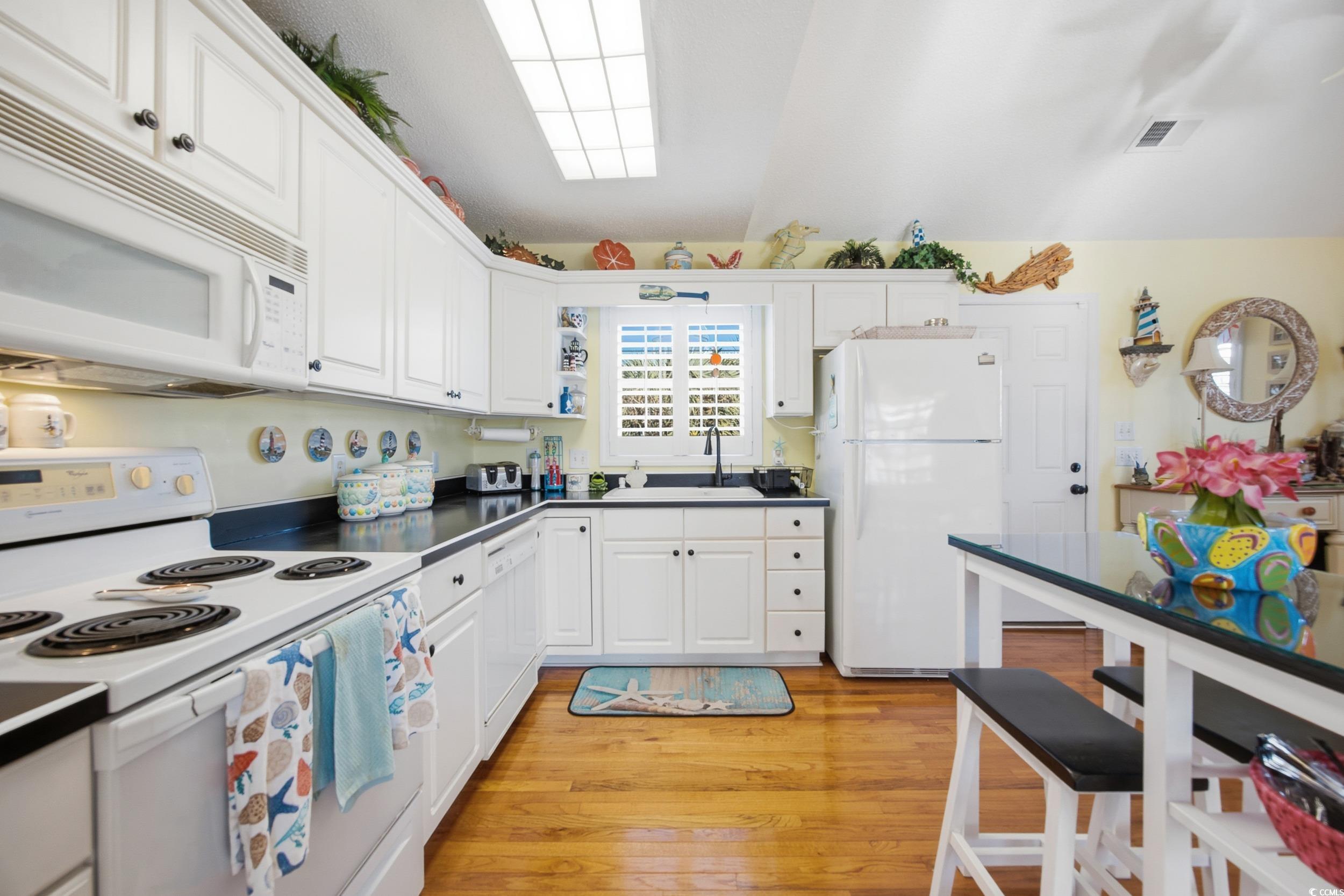 Kitchen featuring white appliances, open shelves, white cabinetry, light wood finished floors, and dark countertops