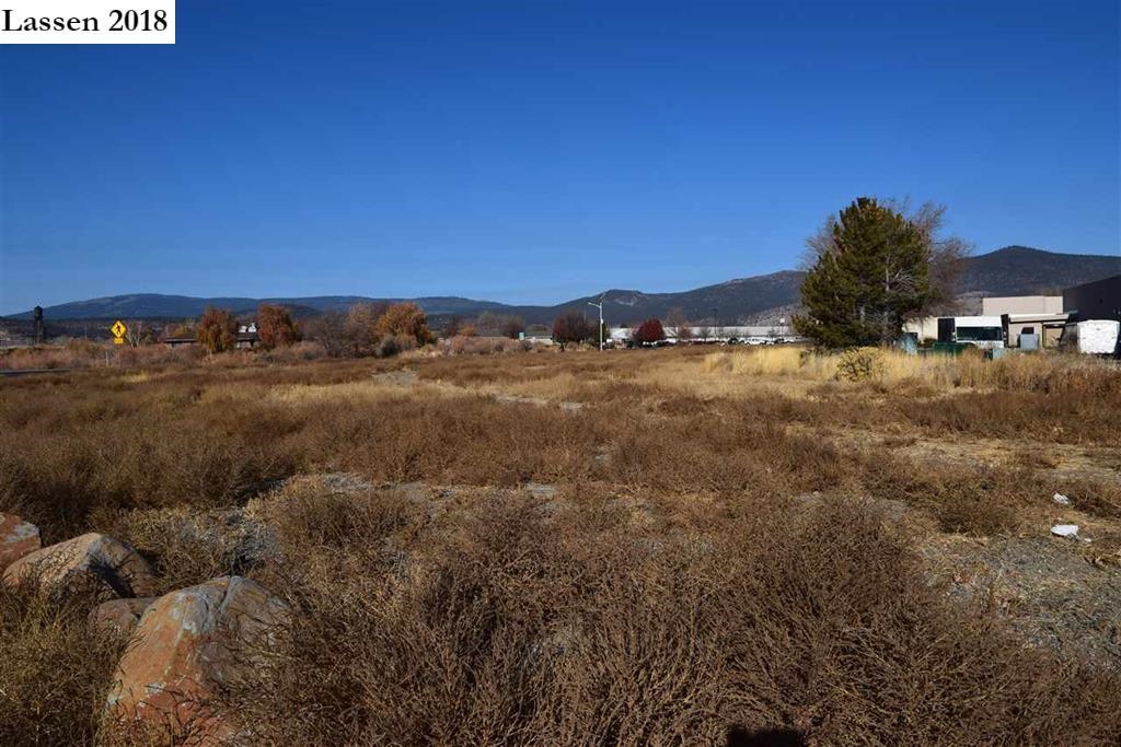 Vacant brush-covered parcel with commercial buildings and mountains in the distance.