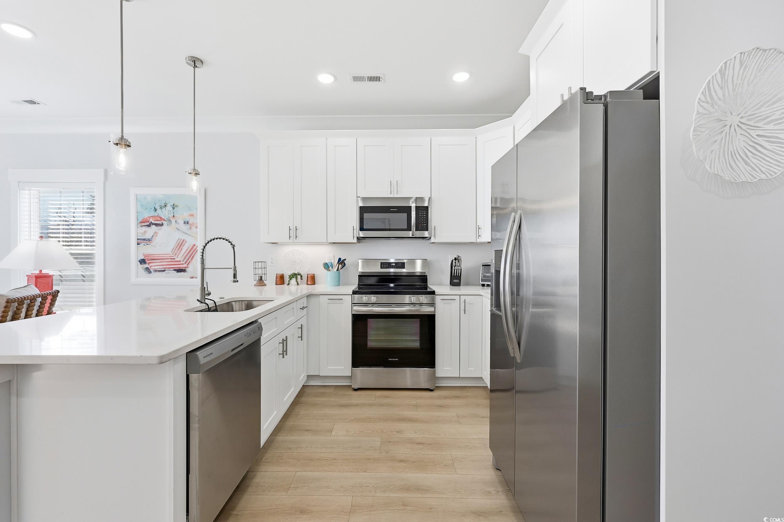 Kitchen featuring appliances with stainless steel finishes, decorative light fixtures, white cabinetry, recessed lighting, and light wood-style floors