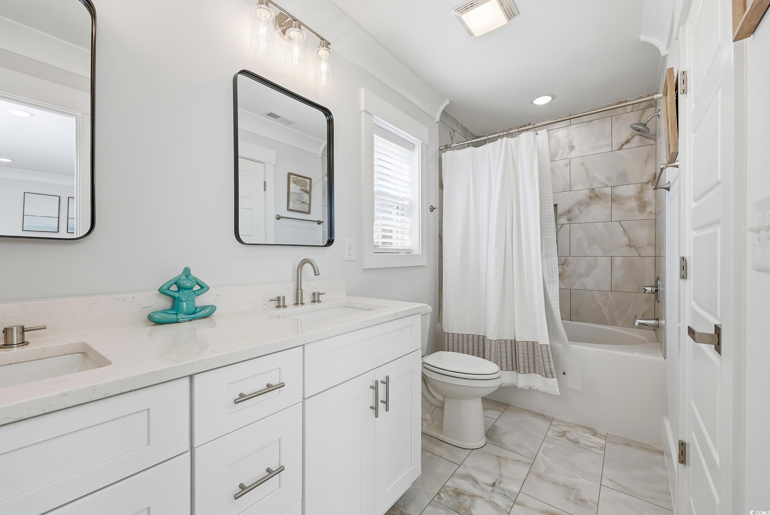 Bathroom with double vanity, shower / tub combo, and light marble finish flooring