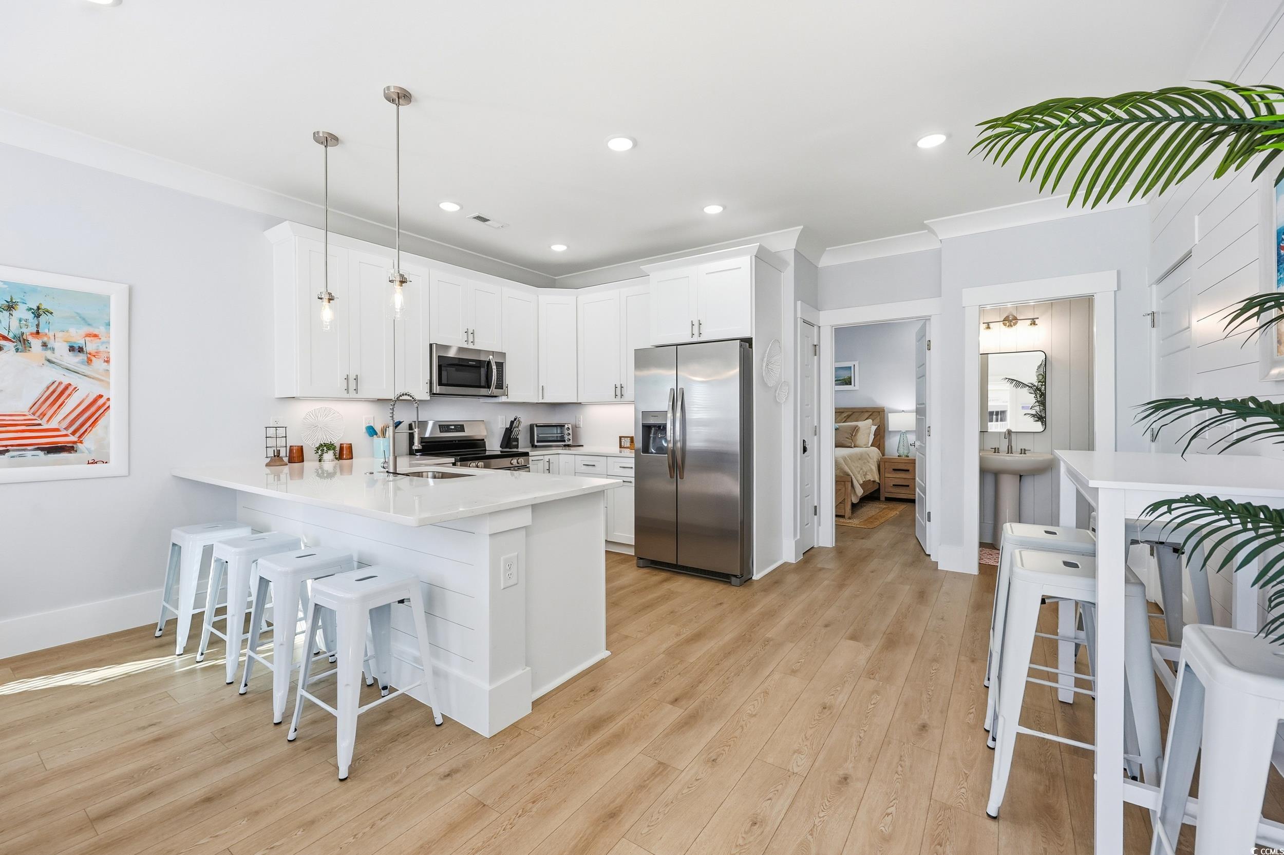 Kitchen featuring a kitchen breakfast bar, stainless steel appliances, pendant lighting, white cabinetry, and ornamental molding