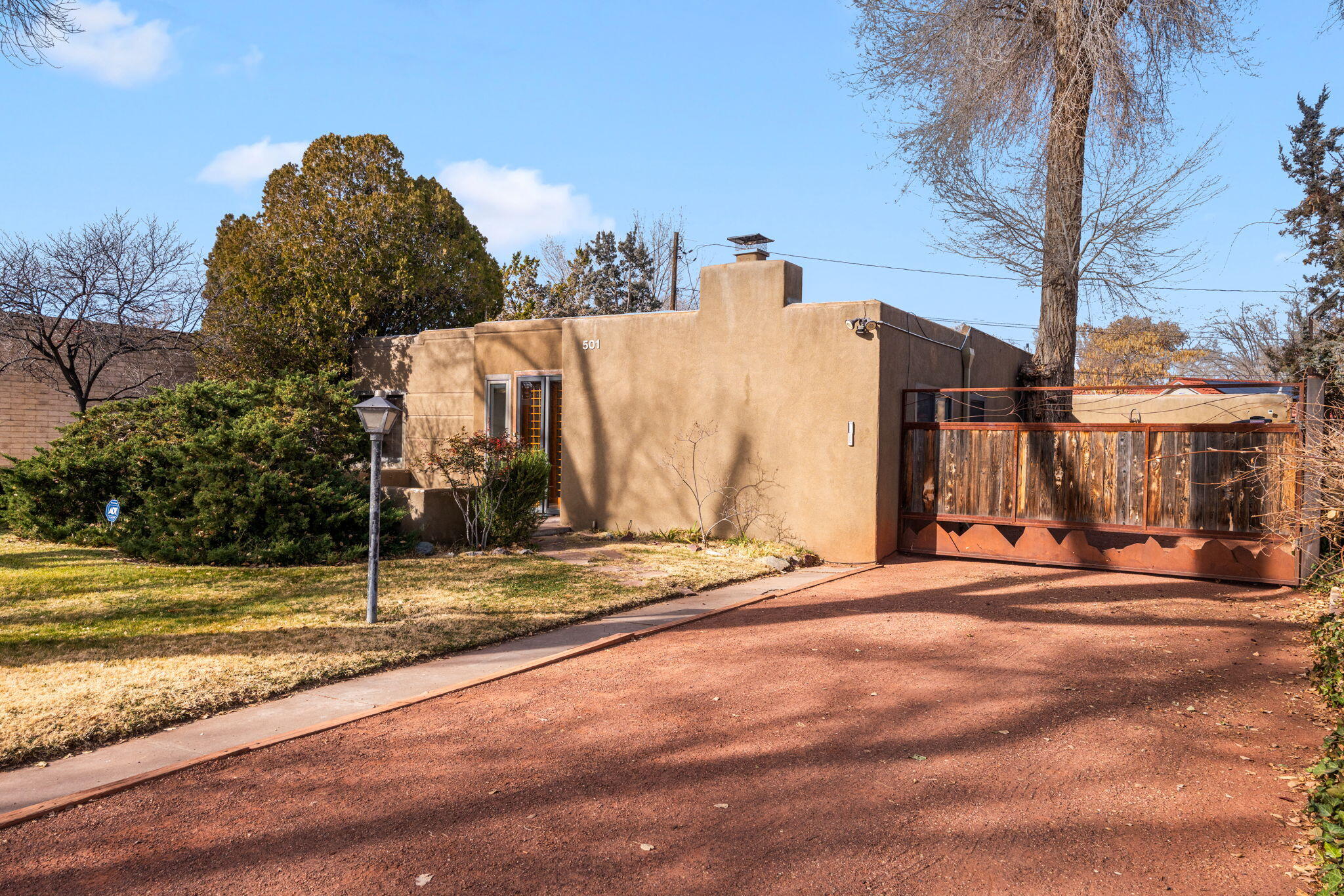 Begin your tour through a custom multi-pane entry door with contemporary flair into sun-filled living spaces featuring hardwood floors and smooth plaster walls. The living room welcomes natural light, while a cozy den near the breakfast room offers a wood-burning fireplace for relaxed evenings. The kitchen is thoughtfully planned with a large pantry and breakfast room.  The private primary suite is tucked away with a kiva fireplace, bookcases, skylight, and a stylish bath with clawfoot tub, separate shower, and a built-in study and inviting sitting area. Enjoy a private courtyard for outdoor dining, an artistic solar-powered driveway gate, and a separate art studio with lighting and mini-split (not inlcuded in sq ft!). All within walking distance to ABQ Country Club.