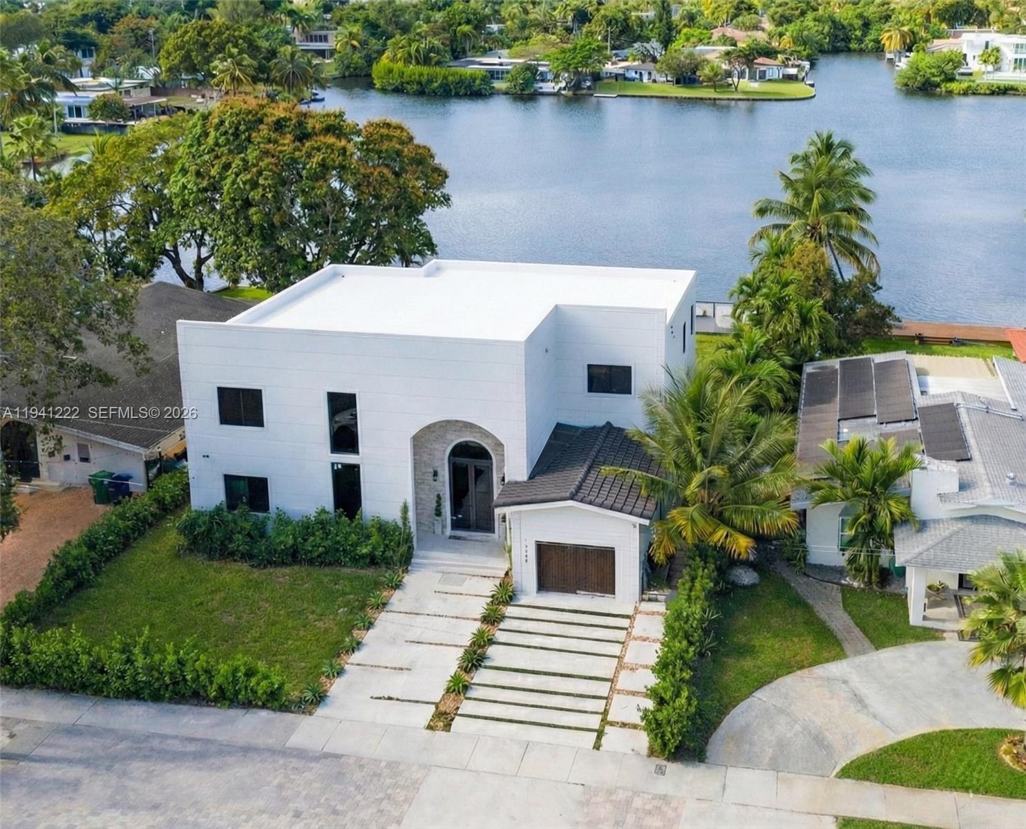 Back to market! Delighted to present this extraordinary newly built waterfront estate, where contemporary architecture, advanced technology and an irreplaceable location converge.Set along a tranquil lake with direct access to the bay, this brand-new residence delivers a refined lifestyle defined by light, volume and effortless sophistication. Soaring ceilings and expansive impact glass flood the interiors with natural light while framing serene water views.The main living spaces flow seamlessly into a bespoke chef’s kitchen featuring custom millwork, premium appliances, an oversized marble island and an elegant butler’s pantry, designed for both everyday living and elevated entertaining.The primary suite is a private sanctuary overlooking the water, complete with a sitting lounge, a custom walk-in closet and a spa-inspired bathroom with freestanding tub, oversized shower and refined stone finishes. Additional bedrooms are generously proportioned with en-suite bathrooms.This smart residence is fully equipped with whole-home audio, a central vacuum system, architectural LED lighting and high-efficiency climate control.Outdoor living features expansive terraces and a private waterfront deck, ideal for entertaining or launching a jet ski with direct bay access.Ideally located, just steps from Aventura Mall, this turnkey waterfront home offers a rare balance of privacy, convenience and prestige.