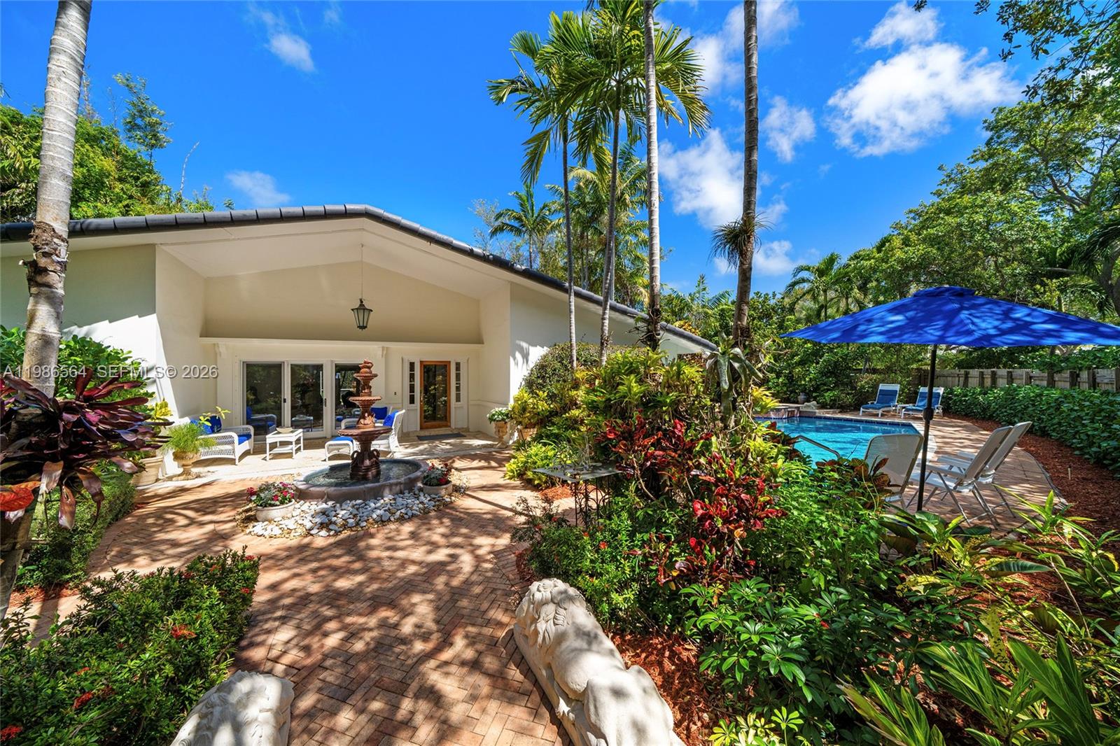 This beautiful villa-style residence in Key Biscayne sits on charming Cranwood Drive, a quiet, residential street lined with mature oak trees near the Village entrance. Home offers 5RB/4BA, including a staff BR with ensuite bath and private entrance. Interior features include classic Cuban tile and parquet hardwood floors, French doors, Thermopane windows, LED lighting, and custom designer millwork. The home presents 3,077 total SF on an elevated 10,007 SF gated lot with wood fence and custom Dade County pine gate. Mature tropical landscaping surrounds the property, and a brick walkway leads to the welcoming fountain entry. Outdoor features include a free-form Bisazza glass pool with 32-ft lap lane and a spacious screened patio lounge with a fountain for a true indoor-outdoor experience. Inside, the spacious living room boasts high ceilings, custom millwork, a wood-burning fireplace, and direct patio lounge access. A private dining area sits next to the gourmet kitchen with a pitched wood-beamed ceiling, large center granite island, top-tier Electrolux, Whirlpool/Profile appliances, plus a breakfast area with a stained-glass window. The private principal suite includes a flexible office/den space, walk-in closet, ensuite bath, and garden access. Three additional bedrooms, including a private guest suite, all overlook lush gardens. This rare offering combines privacy, tropical charm, and exceptional living in one of Key Biscayne’s most desirable locations.