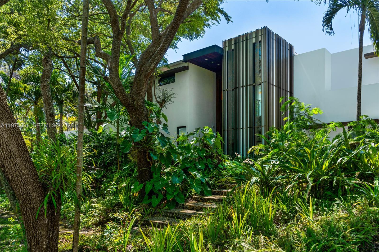 Completed in 2019 by Norway Builders, this exceptional residence sits on a coral ridge along a quiet, tree-lined street on a lush acre lot. Soaring 25+ ft ceilings and expansive open living areas are filled with natural light and overlook a professionally landscaped, resort-style backyard with sparkling pool. Upstairs offers 5 bedrooms, 4 baths, and a family room; the main level includes a VIP guest suite and staff quarters. High-end finishes feature an Italian kitchen and closets, Miele appliances, Spanish stone, oak floors, glass railings, and a dramatic pivot entry door. Per appraisal: 6,267 LA, 7,095 adjusted, 8,989 total. Includes 16kW solar and Tesla battery backup.