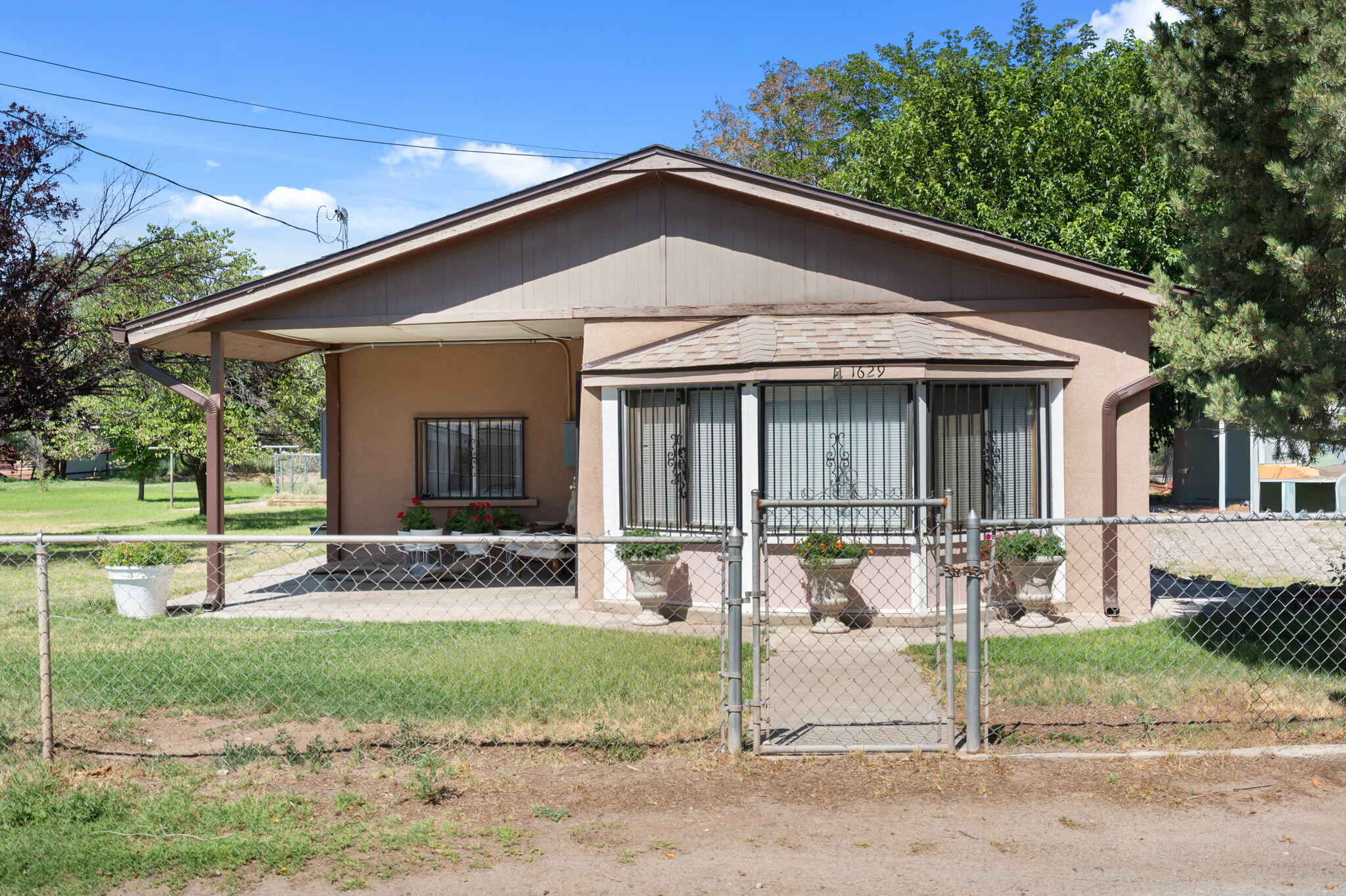 Rare opportunity to own a charming home on nearly an acre in Southwest Albuquerque! This 2-bedroom, 1-bath home sits on a beautiful 0.84-acre lot filled with mature trees and lush grass, creating a peaceful park-like setting with endless possibilities. Enjoy a covered front porch, attractive bay window, and plenty of outdoor space for gardening, entertaining, RV parking, future expansion, or simply relaxing under the shade of the trees. Conveniently located near schools, shopping, dining, and major roadways, this property offers the perfect combination of privacy, space, and city convenience. A unique opportunity with room to grow!