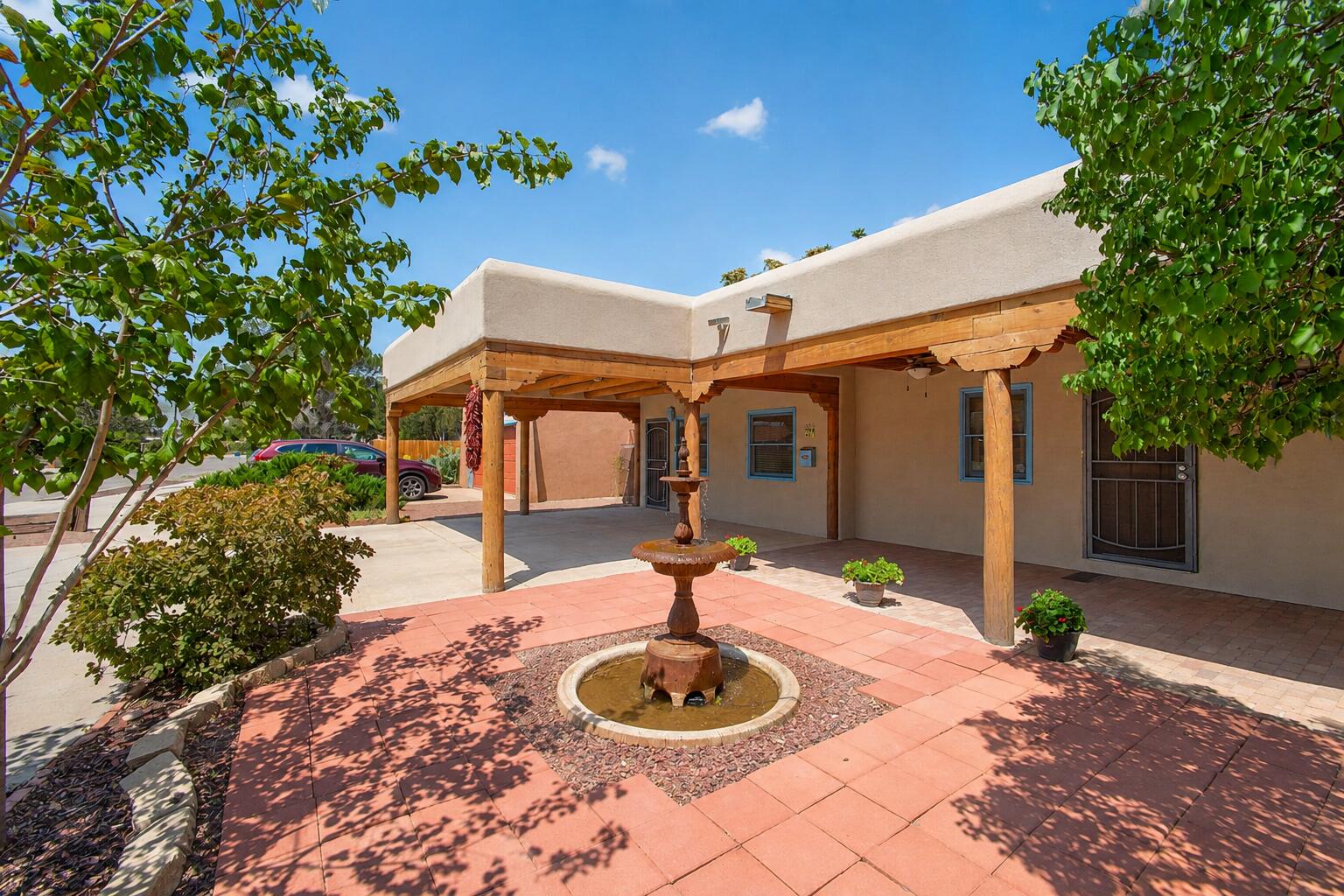 Step through the private courtyard and into a home that feels more like an escape than an address. This distinctive four-bedroom, two-and-a-half-bath with an office, residence combines authentic Southwestern character with unexpected spaces designed for comfort, privacy, and entertaining.Soaring vigas and warm natural wood create a dramatic sense of arrival, while refrigerated air keeps the home comfortable throughout the seasons. Two spacious primary suites offer remarkable flexibility. One becomes its own private retreat with a fireplace, separate living area, and beautiful stained glass imported from England. The second provides another peaceful escape, allowing guests, extended family, or multigenerational living to feel completely at home.The kitchen features granite countertops and flows into generous gathering spaces, while a wet bar makes entertaining effortless. Two fireplaces bring warmth and atmosphere throughout the home, and the spa-inspired bath invites you to unwind in the Jacuzzi tub.Outside, the experience continues beneath a covered portal with soaring vigas, a colorful outdoor kitchen, and custom bancos for relaxed evenings with friends. Removable curtains can enclose the space when desired, while the private hot tub and lush surroundings create the feeling of a secluded resort.An office provides dedicated space to work from home, and exceptional storage includes a separate workroom and additional outdoor storage.This is not simply a home with four bedrooms. It is a collection of experiences: quiet mornings in the courtyard, fireside evenings, outdoor dinners beneath the vigas, and your own private retreat waiting at the end of every day.