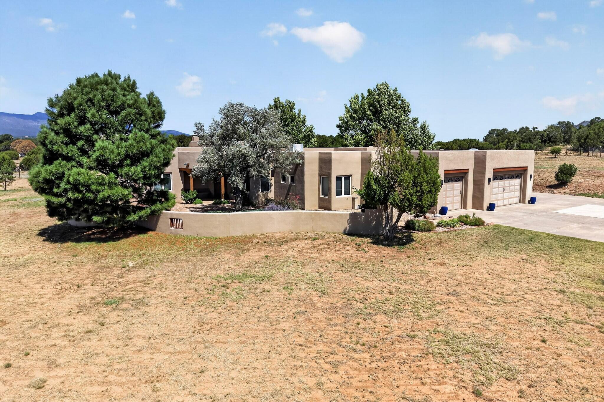 Breathtaking Southwestern-style custom home nestled on 2.66 fully fenced, usable acres, offering privacy, space, spectacular mountain views, and the convenience of being just 10 minutes from Albuquerque. The property features an expanded 3-car garage plus an RV pad. Step inside to a light-filled, open floor plan showcasing 12-foot viga-beam ceilings and a dramatic wall of windows that frame the stunning mountain views. The open chef's kitchen is beautifully appointed with stainless steel appliances, granite countertops, a large island, and custom Halbert cabinetry. The spacious family room features a built-in wet bar and mini fridge, creating the perfect setting for gatherings. The generous primary suite offers a cozy kiva fireplace and flexible bonus space--perfect for a home office or nursery. Secondary bedrooms are generously sized, including one with its own ensuite full bathroom. Step outside to experience exceptional outdoor living, with a built-in BBQ and kiva-style wood-burning fireplace--perfect for enjoying New Mexico sunsets, entertaining guests, and taking in the surrounding mountain scenery. Additional updates include: roof and skylights w/transferable warranty (2022), custom driveway gate w/radio call box, outdoor 4 burner gas grill and more!