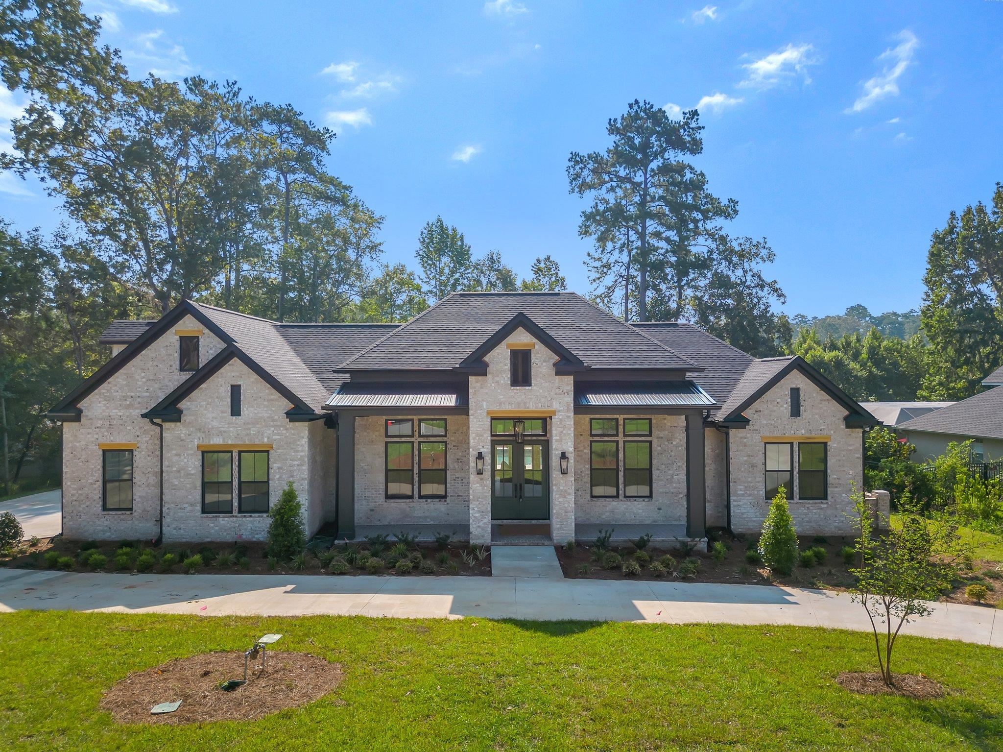 Brick home with a broad gabled roof, landscaped lawn, and mature trees behind it.