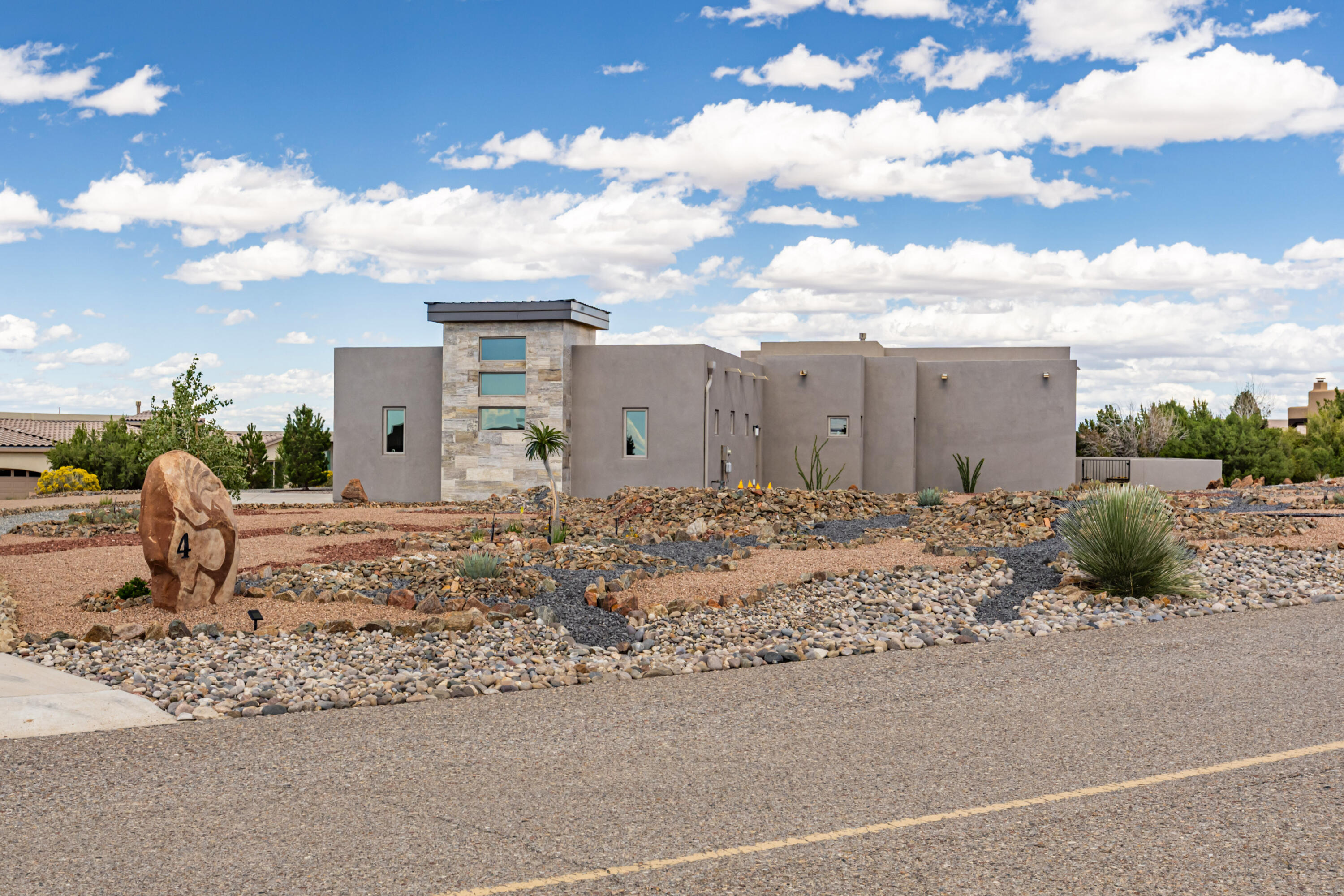 An exceptionally well maintained, mid-century design with a  light and bright floor plan on this 2023 constructed home in Anasazi Meadows. The lot is on the highest plateau in the immediate neighborhood enabling those spectacular views of the Sandia mountain and mesa sunsets. Great room design with large southern windows, raised ceiling, wood plank/ceramic floors, tiled wall  accents, gas fireplace and wood beams. Kitchen area with custom cabinets, granite counters, stainless appliances, walk in butlers pantry and large island allowing ease of cooking while still being roomy. Private master bedroom suite has patio access, mountain views, his/hers walk in closets, separate vanity areas, snail shower, high back tub, and immediate access to the laundry room. The two separate bedrooms have a Jack N Jill bath where each bedroom has a sink and closet with the toilet and tub shared. The gigantic three car garage has room for a workout area and a work shop with an enamel floor and flooded with natural light. The culmination of this special property is a most unique rock landscape which highlight Southwestern, Native American and Hawaiian design features such as figures of geckos, sun signs and volcano with lava flows. These intricate icons with engineered drainage and erosion control make this landscaped yard truly 'one of a kind'.