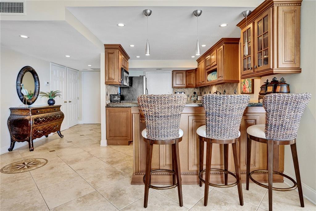 A beautiful tile custom designed entry medallion is part of the neutral porcelain tile, which runs thru out the apartment. Pendant lighting is above the kitchen eat in granite top counter area. Note the two closets in the entry way: One of them houses the washing machine and dryer.