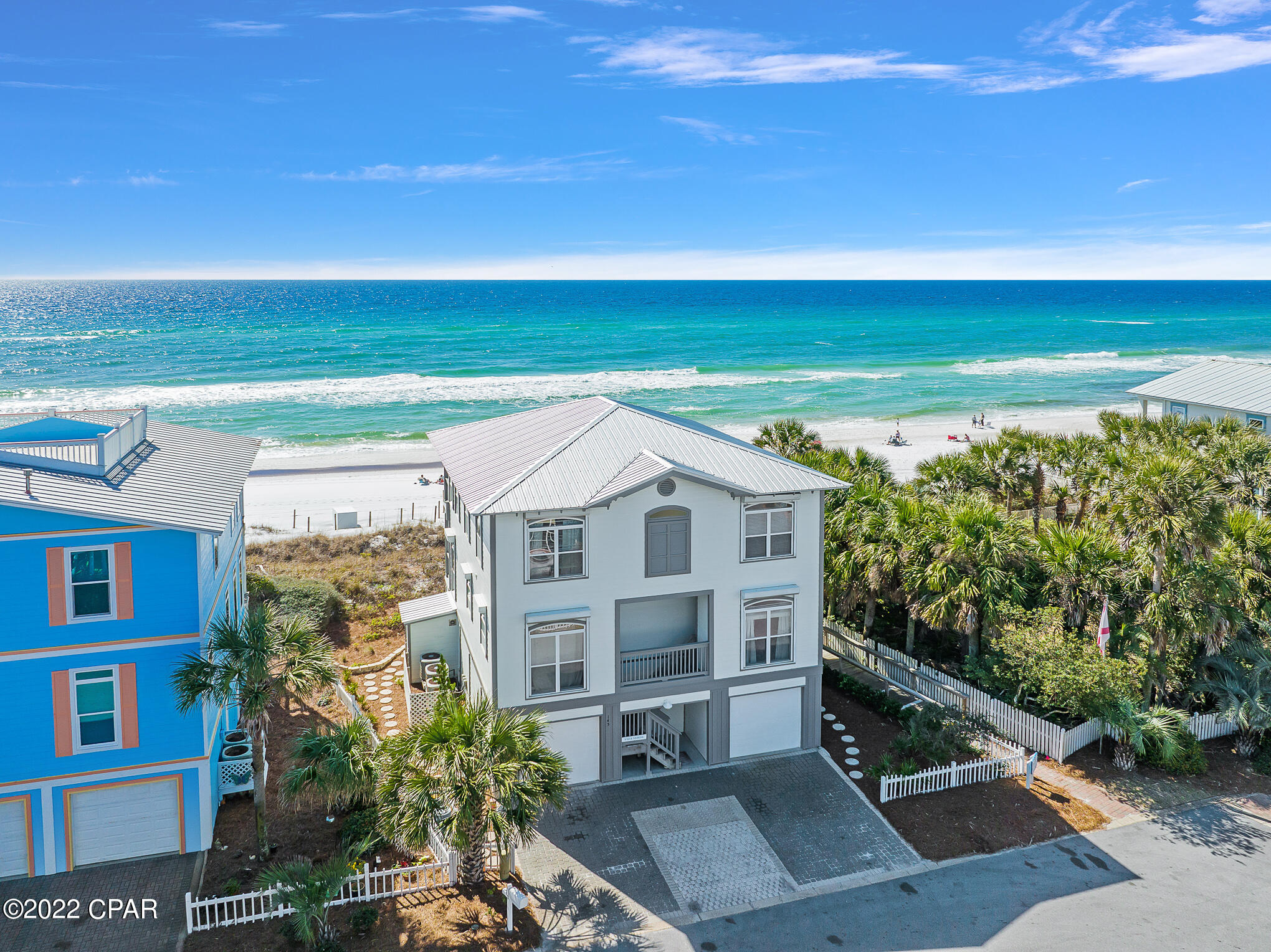 Beachfront homes beside white sand and turquoise Gulf water, seen from above.