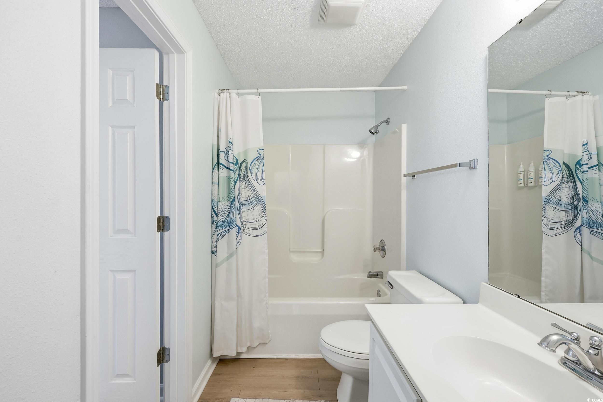Bathroom featuring shower / bath combination with curtain, vanity, a textured ceiling, and light wood-style flooring