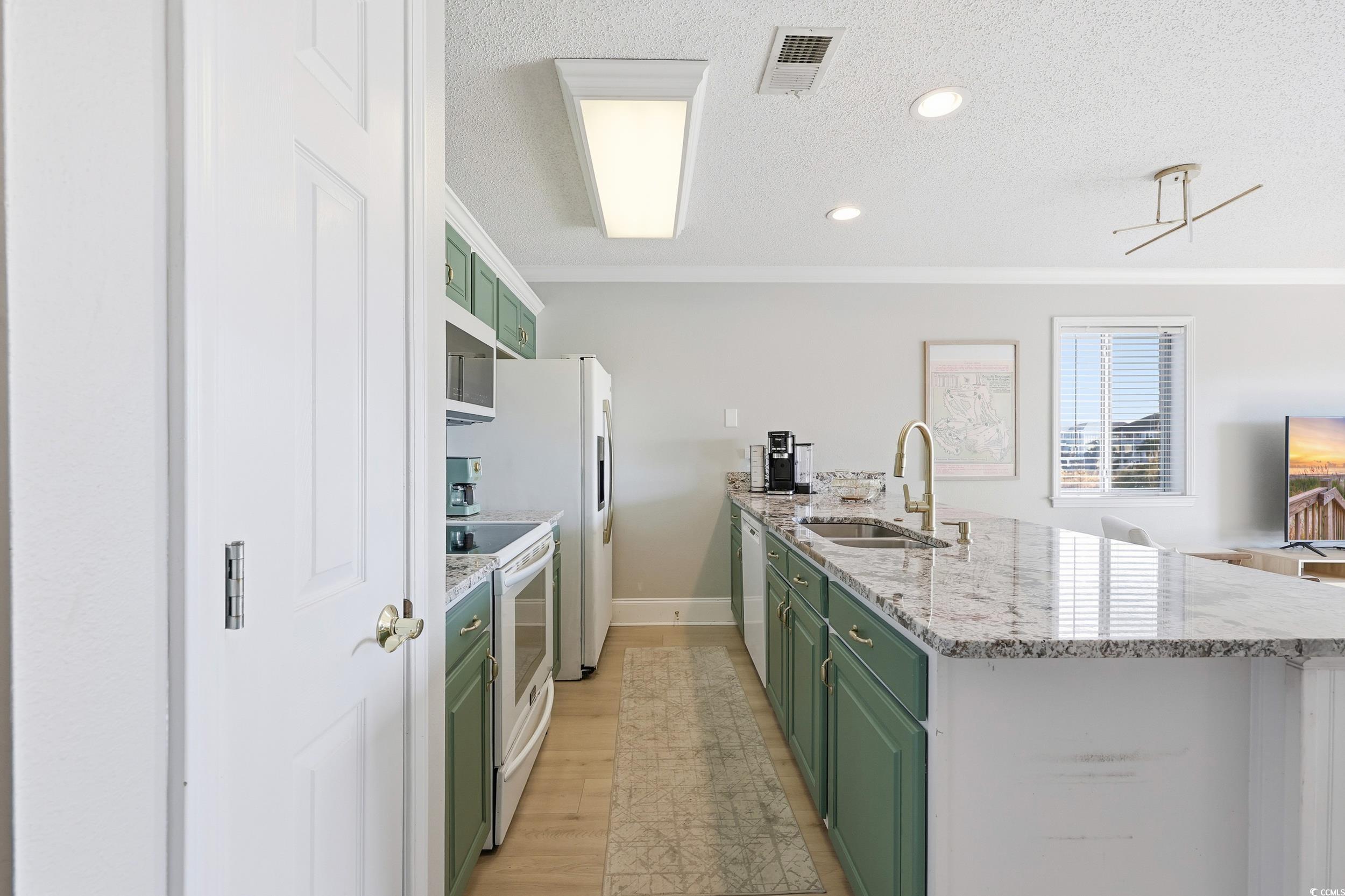 Kitchen with green cabinetry, light stone counters, white appliances, a peninsula, and a textured ceiling