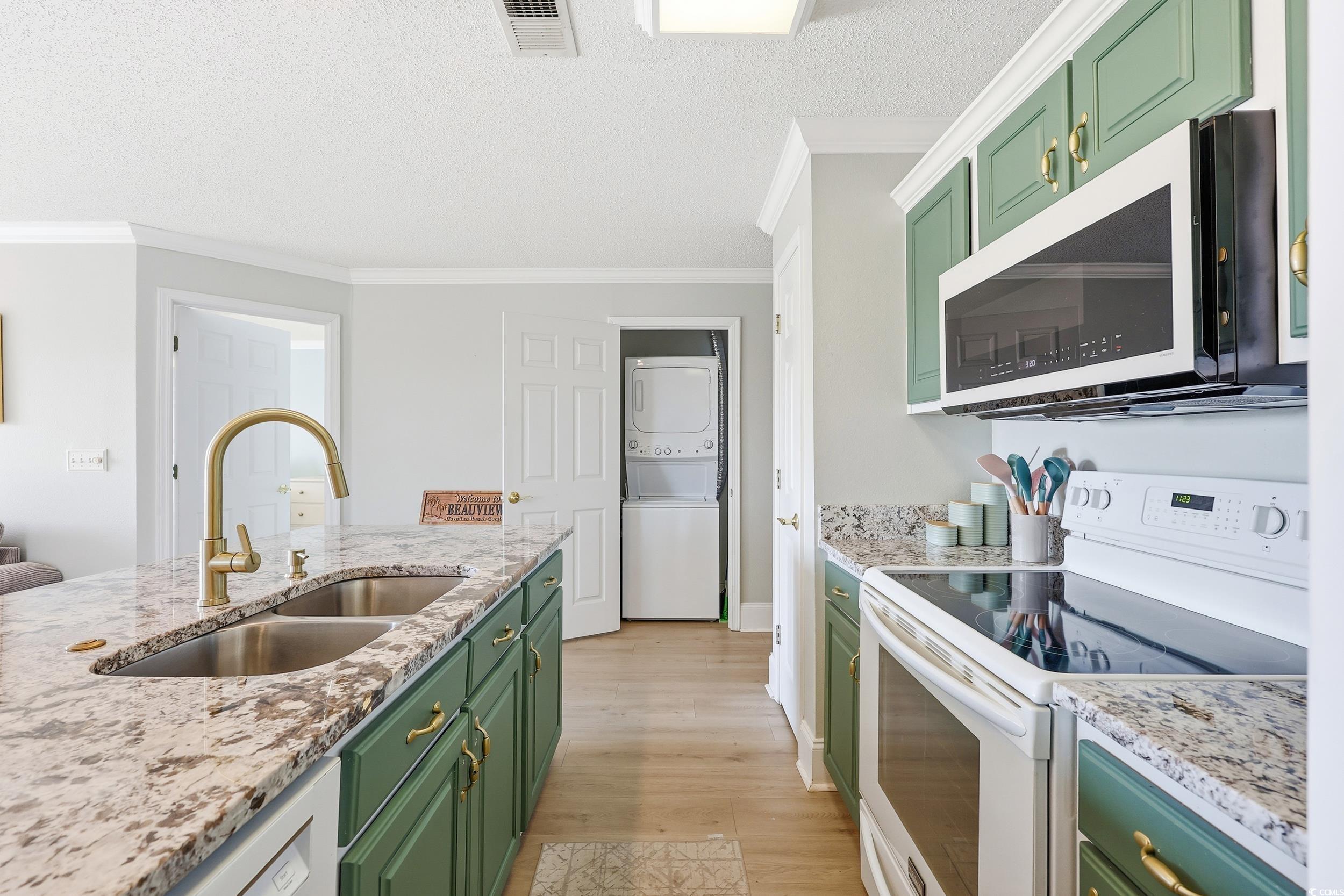Kitchen featuring green cabinetry, white range with electric cooktop, stainless steel microwave, light stone countertops, and crown molding