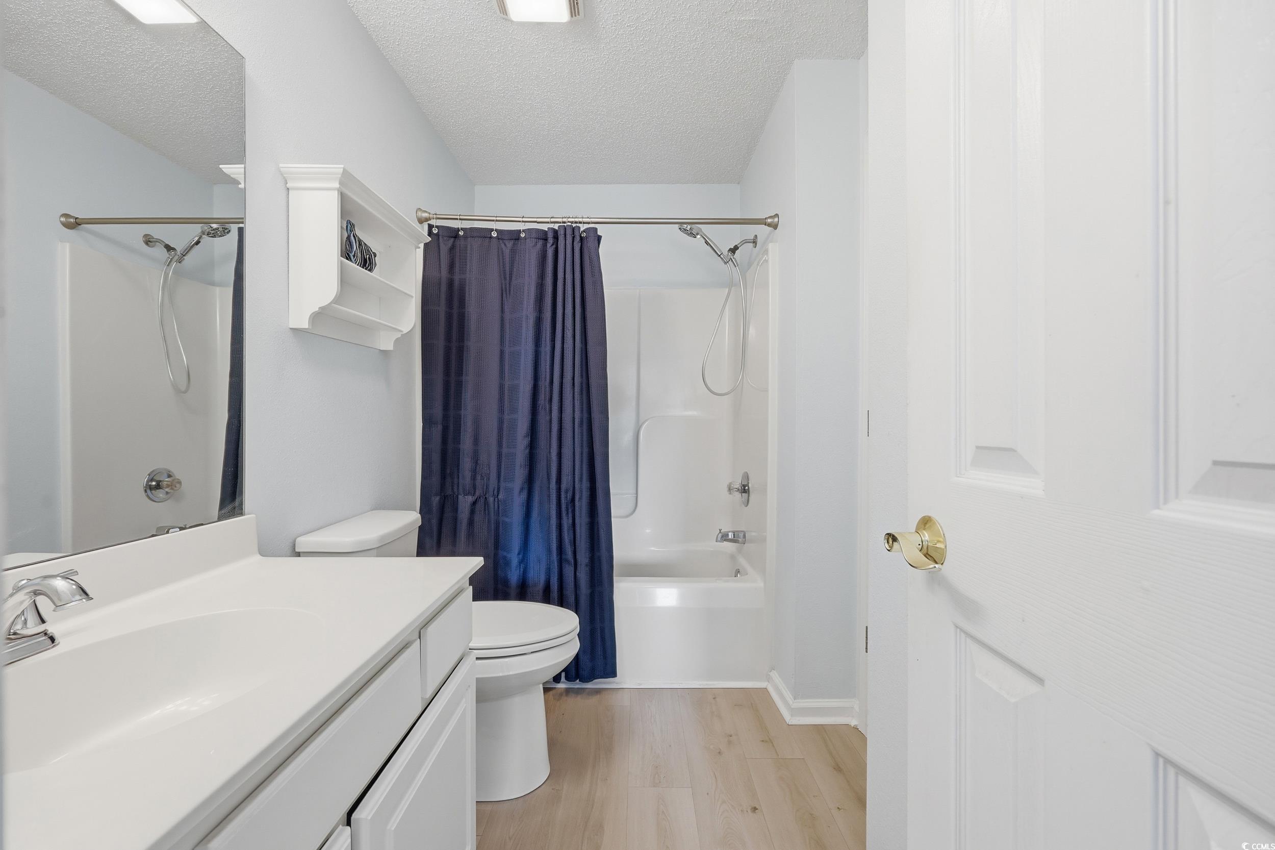 Bathroom with shower / bathtub combination with curtain, a textured ceiling, vanity, and light wood-style floors