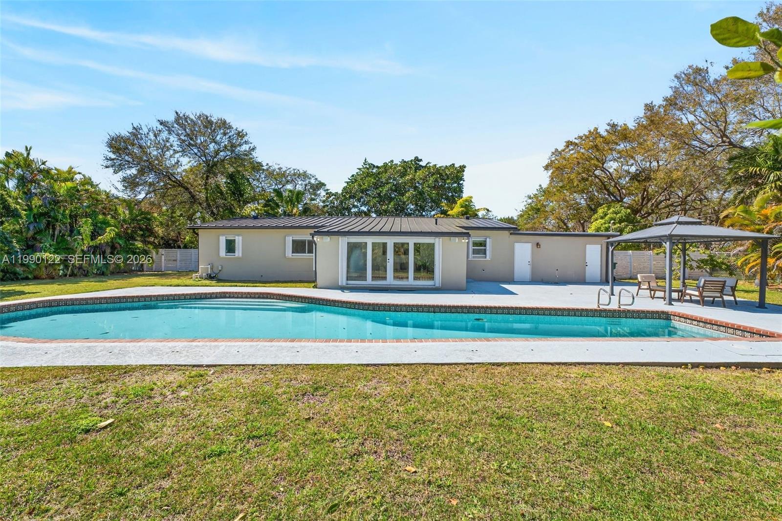 A move-in ready sanctuary sitting on a sprawling 19,710 SF lot, offering exceptional privacy and tranquility surrounded in nature within Miami’s most desirable neighborhoods. A gated courtyard entry welcomes you into light-filled interiors and a seamless open floor plan designed for both everyday living and effortless entertaining. The centrally positioned kitchen features white cabinetry and a striking quartz waterfall countertop, flowing into generous living areas. Recent upgrades include a new metal roof, resurfaced pool and pool pump. A spacious laundry room and garage add convenience and storage. Outdoors, an oversized open pool with original Spanish tiles anchors the expansive, fully fenced backyard with ample room to expand or customize. Front and back yards have mature vegetation with unique trees like the ponytail palm and fire tree, as well as mango, sapodilla, jackfruit, and avocado trees. Ideally located near top-rated schools, parks, shopping, and dining, this home offers refined Pinecrest living.