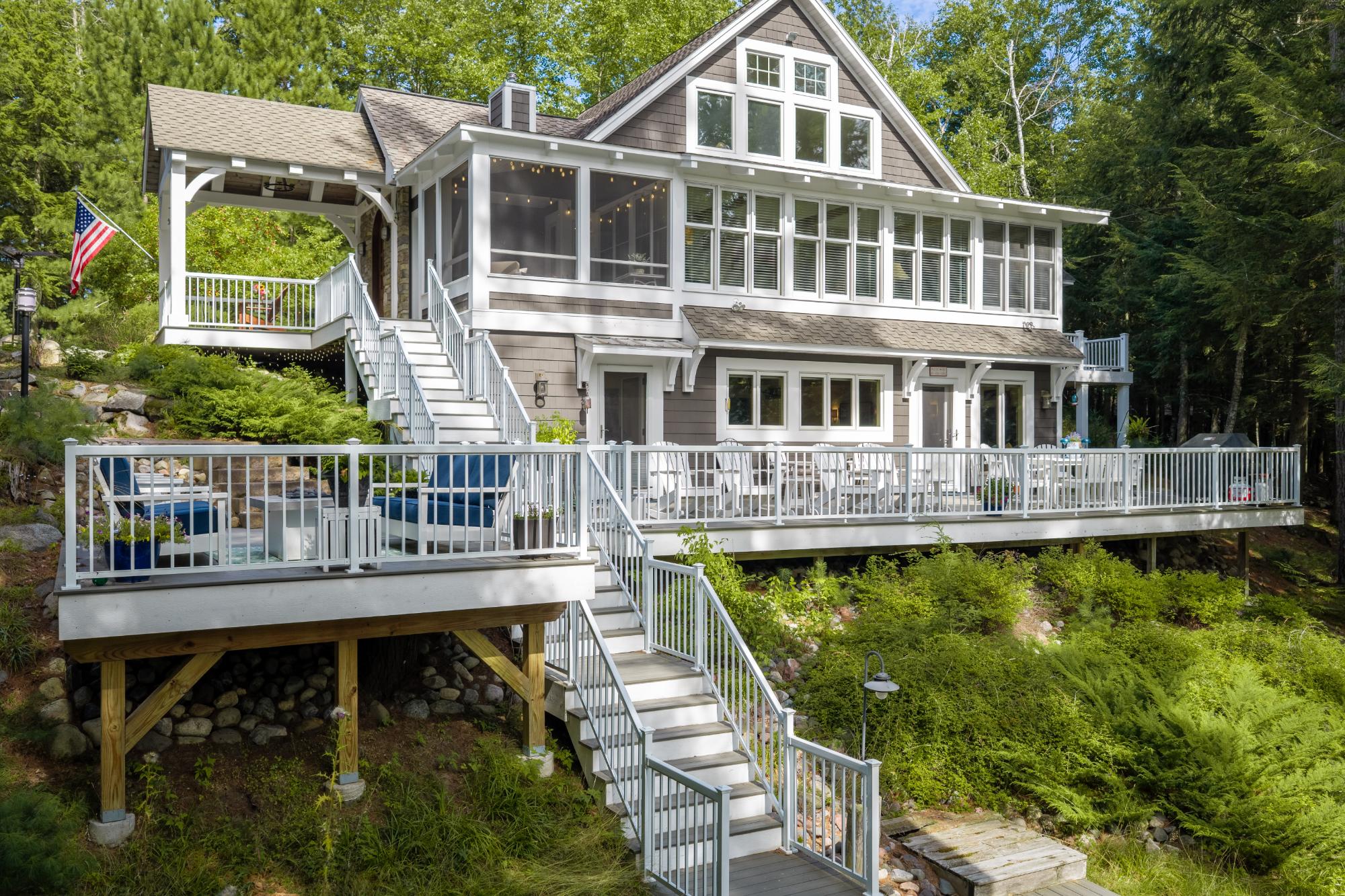 Gray-and-white home with a screened porch, tiered decks, and long staircases in a wooded setting.