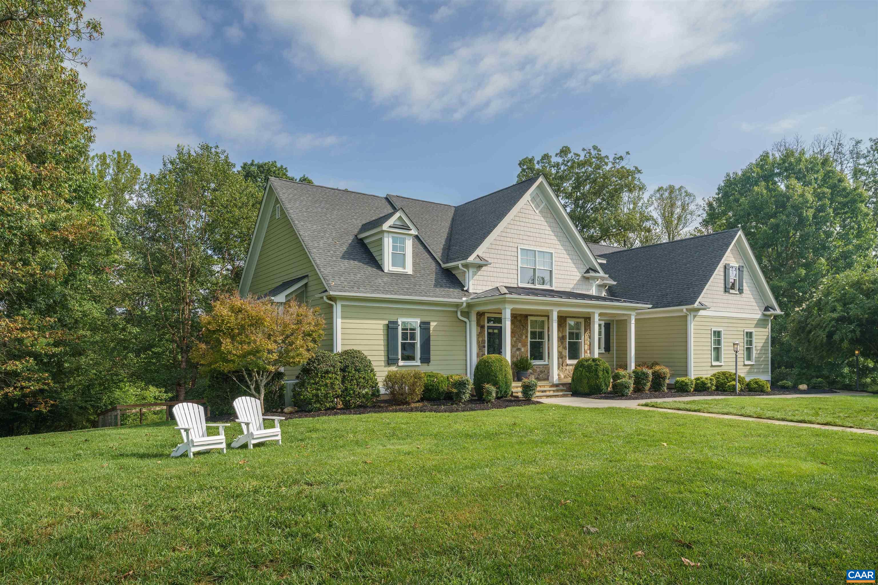 Green-and-cream gabled house with a stone-accented porch, broad lawn, and two white Adirondack chairs.